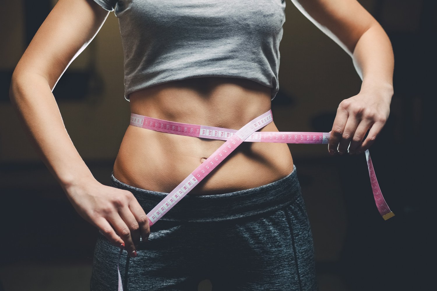 Slim girl bodybuilder centimeter measuring her waist in a gym.